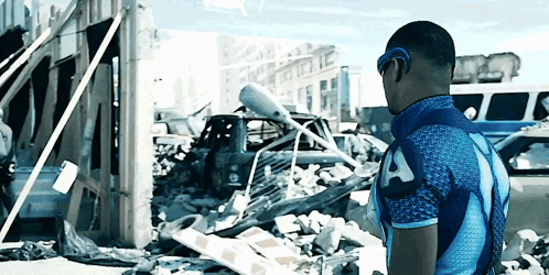 Man In Blue Shirt With Letter A In Front Of Destroyed Building GIF