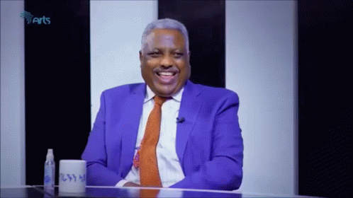 Man In Blue Suit And Orange Tie Smiling With Cup GIF