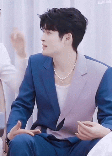 Man In Blue Suit And Pearl Necklace Talking To Another Man GIF