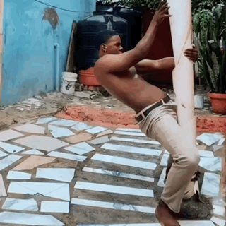 Man In Blue Sweater And White Pants By Parking Lot Fence GIF