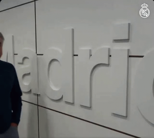 Man in Blue Sweater in Front of Wall Saying Madrid