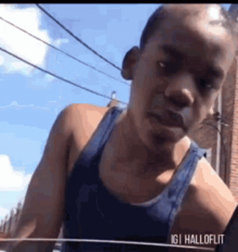 Man In Blue Tank Top In Front Of Brick Building GIF