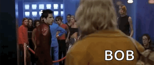 Man In Brown Jacket With Bob On Back In Crowd GIF