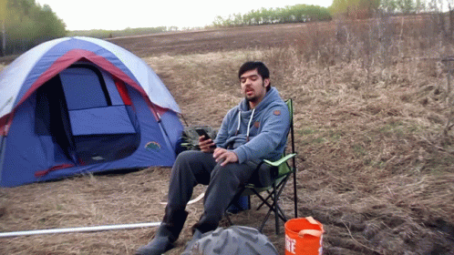 Man In Chair In Front Of Tent With Fire Bucket GIF