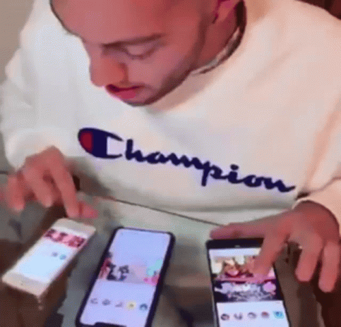 Man in Champion Sweatshirt Looking at Two Phones