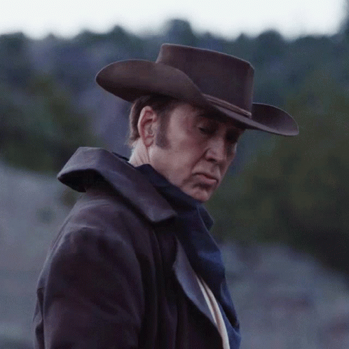 Man in Cowboy Hat and Coat Looks Down