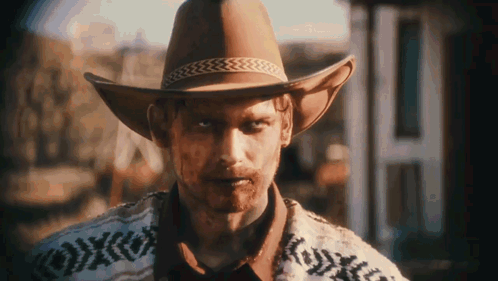 Man In Cowboy Hat And Sweater In Front Of Building GIF