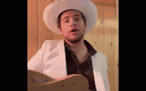 Man In Cowboy Hat And White Jacket Holding Guitar GIF