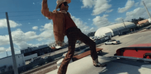 Man in Cowboy Hat Standing on Car Roof