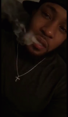 Man In Cross Necklace Smoking In Dark Room GIF
