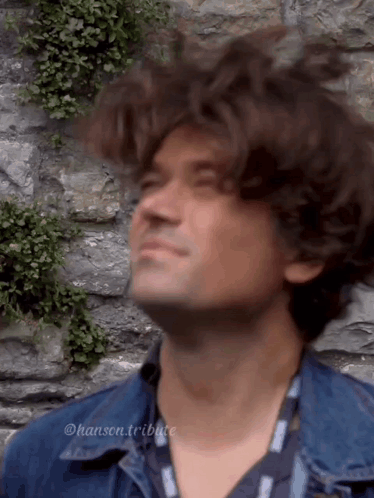Man in Denim Jacket Looking Up at Stone Wall