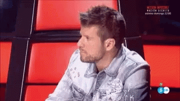 Man in Denim Jacket Sitting in Chair with Red Cushions