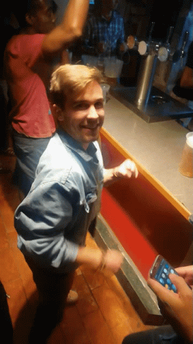 Man In Denim Shirt At Bar With Man In Red Shirt Behind GIF
