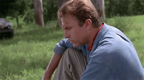 Man In Denim Shirt Sitting On Grass Looking Down GIF