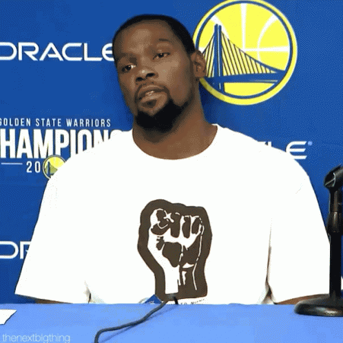 Man In Fist T-Shirt In Front Of Warriors Logo GIF