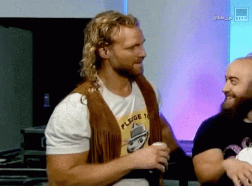 Man In Fringed Vest And Pledge T-Shirt With Another Man GIF