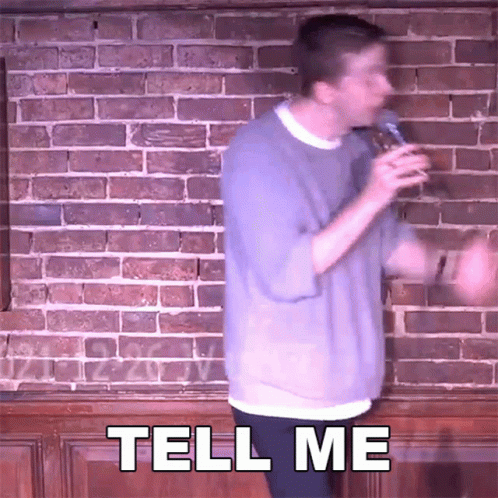 Man in Front of Brick Wall Holding Microphone Says Tell Me