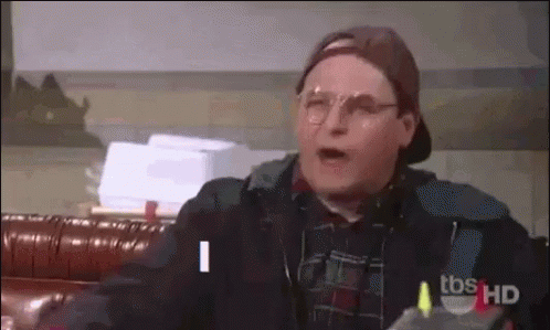 Man In Glasses And Baseball Cap Talking On Couch GIF