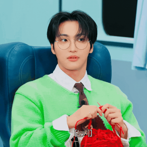 Man in Glasses and Green Sweater Knitting Red Item