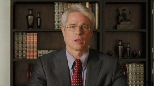Man in Glasses and Suit in Front of Bookshelf