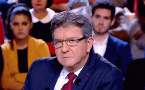 Man in Glasses and Suit Sitting in Front of Crowd