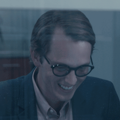 Man in Glasses and Suit Smiling in Dark Room