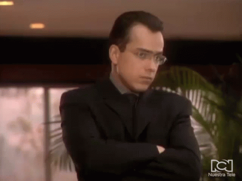Man In Glasses And Suit With Arms Crossed In Front Of Nuestra Tele Logo GIF