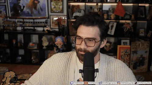 Man in Glasses and Sweater Talking Into Microphone With Hasanab Sign