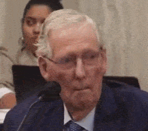 Man In Glasses And Tan Coat Sitting In Blue Chair GIF