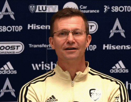Man In Glasses And Yellow Adidas Shirt In Front Of Ad Wall For Hisen Sbotop And Wish GIF