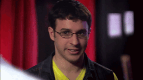 Man in Glasses and Yellow Smiling Before Red Curtain