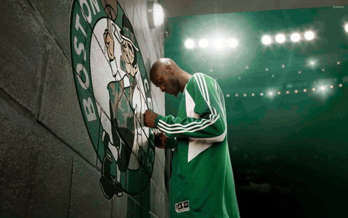 Man In Green Adidas Jacket In Front Of Boston Celtics Logo GIF