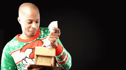 Man In Green And Red Sweater Holding Gingerbread House GIF