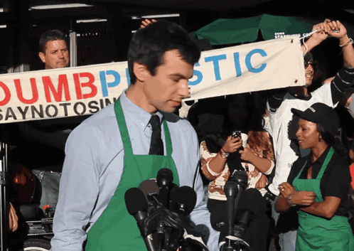 Man in Green Apron Holding Dumbplastic Banner