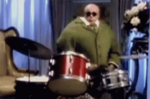 Man In Green Coat Playing Drum Set GIF