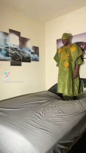 Man in Green Dress Standing on Bed With Cars Wall
