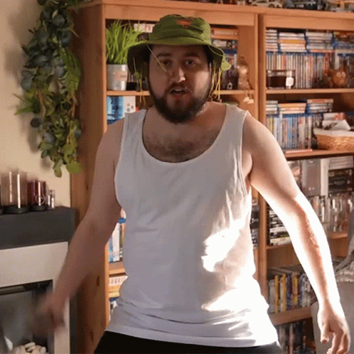Man In Green Hat And White Tank Top By Bookshelf GIF