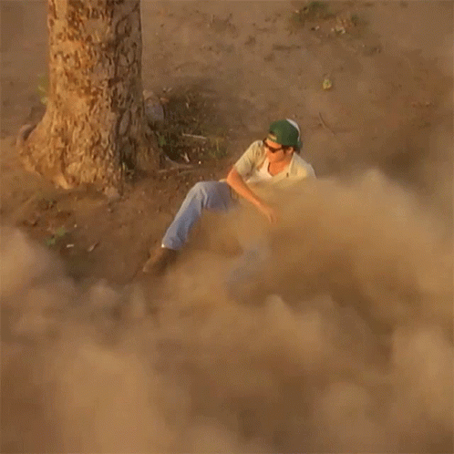 Man in Green Hat Sitting in Dust Near Tree