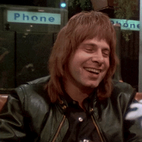 Man in Green Leather Jacket Smiling in Front of Phone Booth