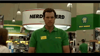 Man in Green Nerd Shirt in Front of Sign Saying Buy More