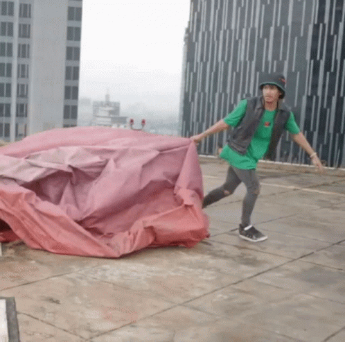 Man in Green Shirt and Black Hat Holding Red Tarp