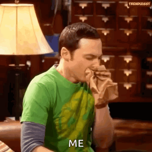 Man in Green Shirt Eating Sandwich Saying Me