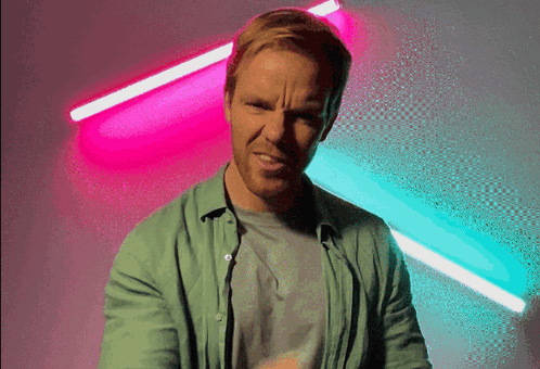 Man in Green Shirt Making Funny Face in Front of Neon Lights