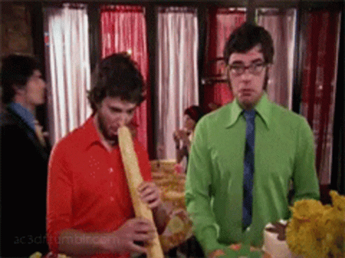 Man In Green Shirt Smoking Cigarette Next To Man In Red Shirt GIF