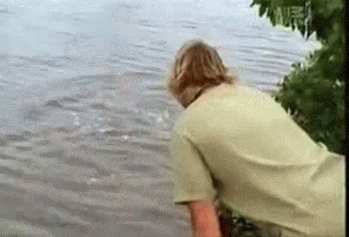 Man in Green Shirt Standing in Water Looking at Shark