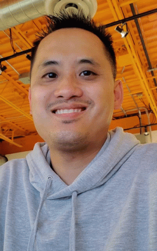 Man in Grey Hoodie Smiling Under Orange Ceiling