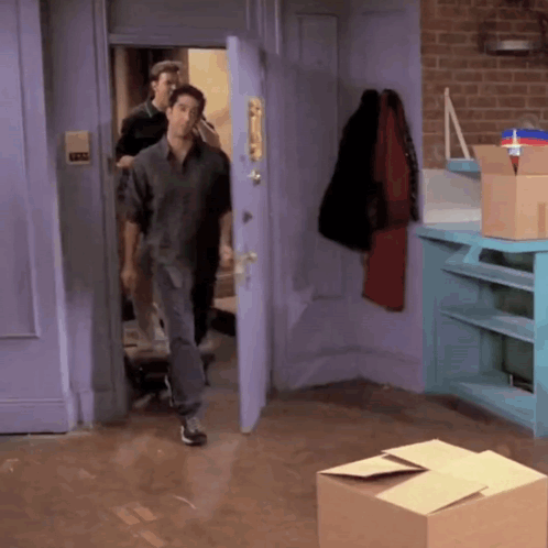 Man in Grey Shirt Walking Into Room With Boxes