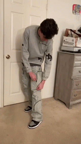 Man In Grey Sweatshirt And Cargo Pants Standing In Front Of Door GIF