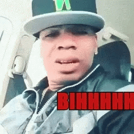 Man in Hat and Jacket in Car With Bihhhh in Red