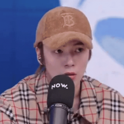 Man in Hat and Plaid Shirt Sitting at Microphone